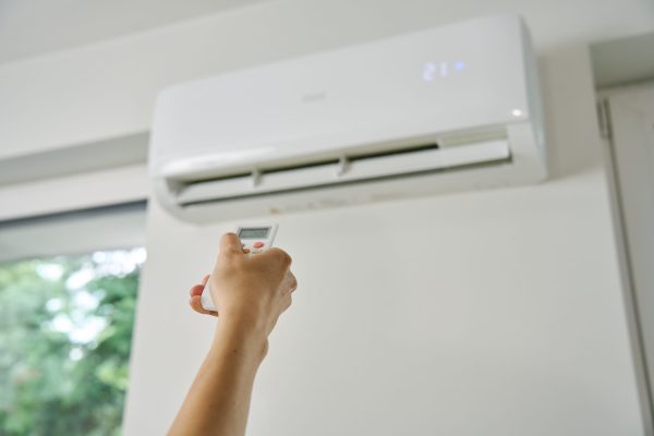Adjusting air conditioner temperature with remote control. Hand holds remote control and setting comfortable temperature on climate system in apartment