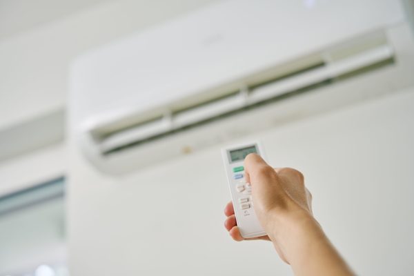 Adjusting air conditioner temperature with remote control. Hand holds remote control and setting comfortable temperature on climate system in apartment