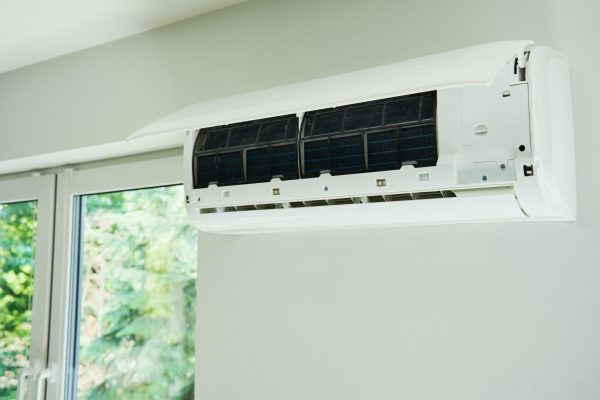White air conditioner unit is mounted on wall, ready for maintenance. Climate system with opened front cover revealing internal components. Repairing HVAC in apartment