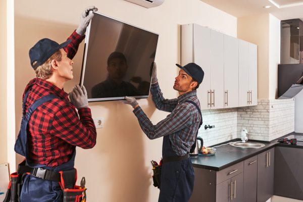 Dismantling of electronics equipment. Two technician remove plasma television in kitchen of customer. Senior mechanic with young trainee